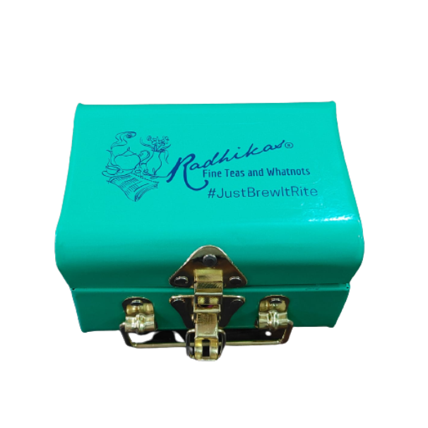 A blue metal tea trunk with the brand name 'Radhikas Fine Teas and Whatnots' and the hashtag 'Just Brew It' on the lid. It has a shiny metal clasp on the front.