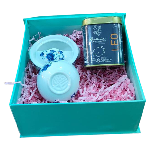 A gift box containing a white ceramic Gaiwan with a blue floral pattern, a small container of tea, and pink tissue paper.