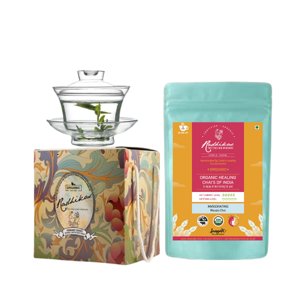 A glass gaiwan set with a saucer and a lid, accompanied by a pack of Radhikas Fine Teas Assam Masala Tea. The gaiwan has a floral design on the packaging.