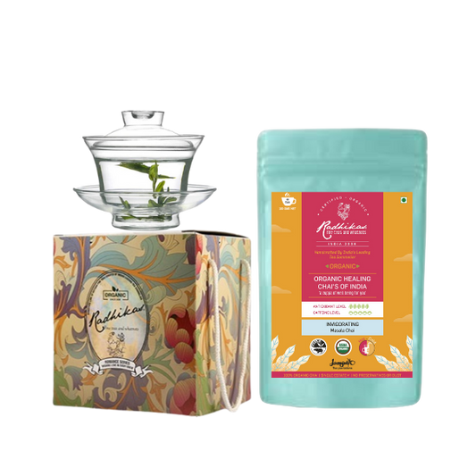 A glass gaiwan set with a saucer and a lid, accompanied by a pack of Radhikas Fine Teas Assam Masala Tea. The gaiwan has a floral design on the packaging.