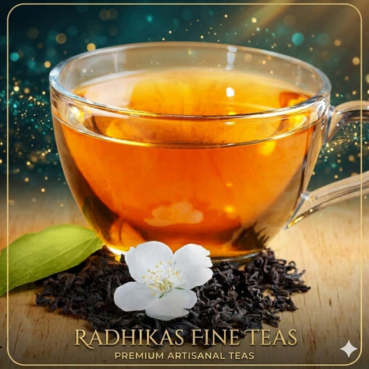 Glass cup of tea with tea leaves and a flower on a wooden surface, featuring Radhika's Fine Teas branding.
