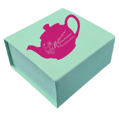 A rigid rectangular gift box with a pink lid, featuring a printed design of a pink teapot and the text 'Radhikas Fine Teas'.