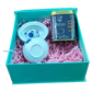 A gift box containing a white ceramic Gaiwan with a blue floral pattern, a small container of tea, and pink tissue paper.