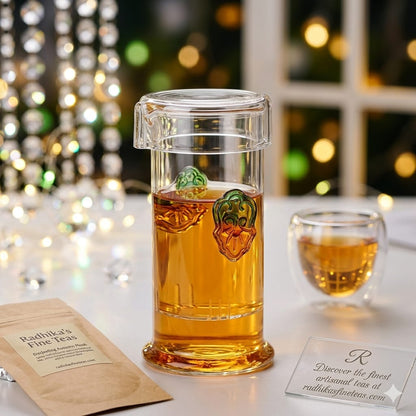 Clear glass mug with tea and decorative lid on a table with blurred lights in the background