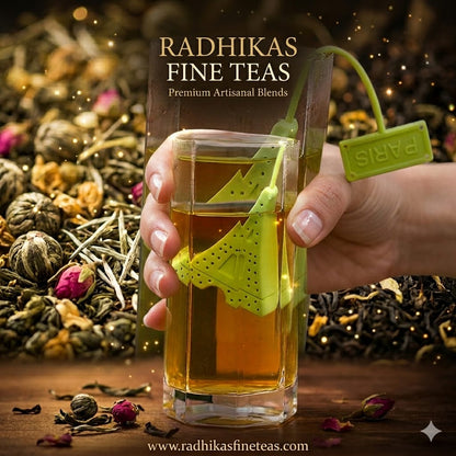 Hand holding a glass of tea with a green tea bag, surrounded by various types of tea leaves, with 'Radhikas Fine Teas' branding.