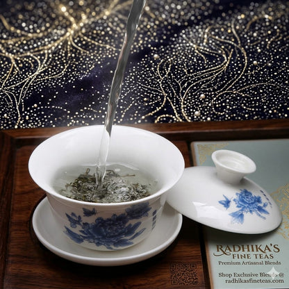 Tea being poured into a blue and white teacup with a lid on a decorative surface.