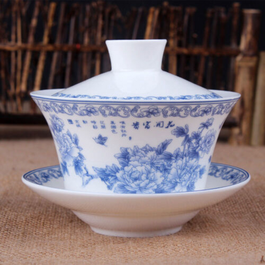 A white porcelain Gaiwan cup with blue floral print, including a lid and a saucer, displayed on a textured fabric.