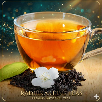 Glass cup of tea with tea leaves and a flower on a wooden surface, featuring Radhika's Fine Teas branding.