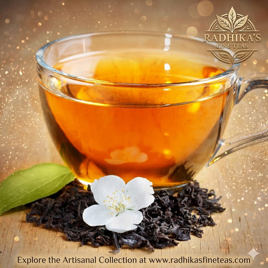 Glass cup of tea with tea leaves and a flower on a wooden surface, featuring Radhika's Fine Teas branding.
