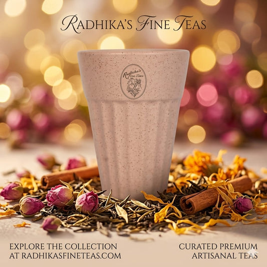 Ceramic cup with 'Radhika's Fine Teas' branding surrounded by tea leaves and flowers on a blurred background.