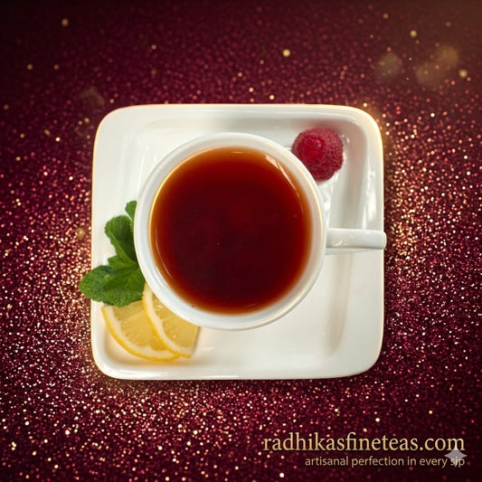White cup of tea with lemon and raspberry on a white square plate against a glittery red background, featuring Radhika's Fine Teas branding.