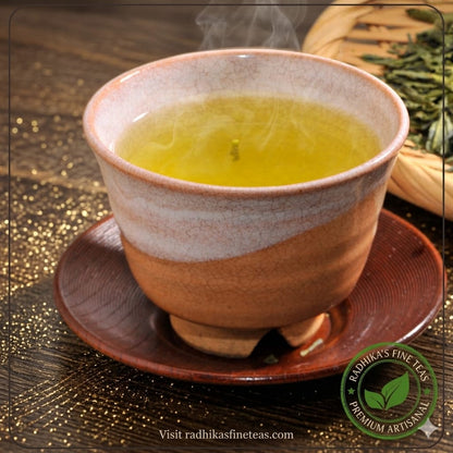 Ceramic cup of green tea with steam on a wooden surface, featuring Radhika's Fine Teas logo.