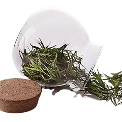 A clear glass jar with a bamboo lid filled with green tea leaves, alongside an empty bamboo lid.