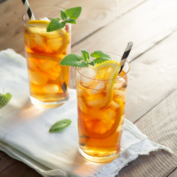 Two glasses of iced tea with lemon slices and mint leaves on a wooden surface.