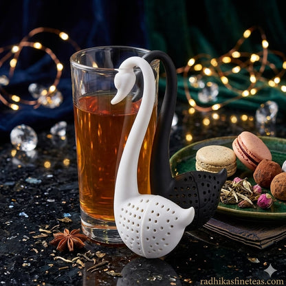 Tea infuser shaped like a swan on a glass of tea with decorative lights in the background.