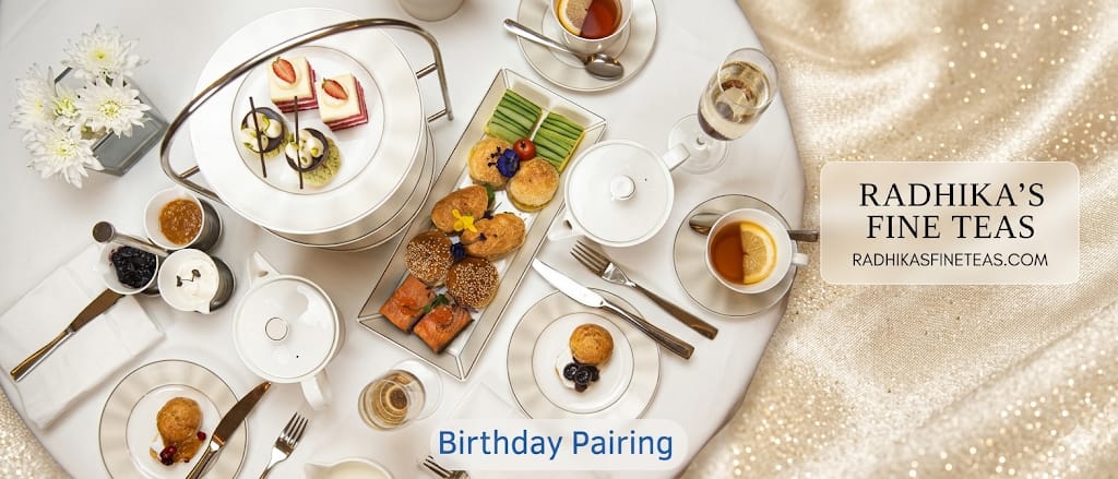 Catered tea service with pastries and tea cups on a white tablecloth, featuring Radhika's Fine Teas branding.