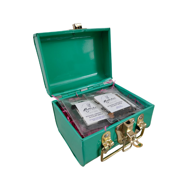 A green trunk with the lid open, containing packets of tea leaves and a strainer.