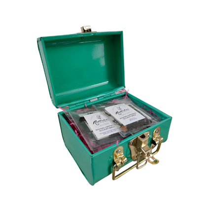 A green trunk with the lid open, containing packets of tea leaves and a strainer.