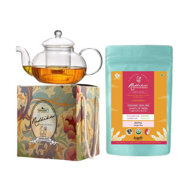 A Victorian glass kettle with a lid next to a packaged tea product, all presented on a decorative box with floral designs.