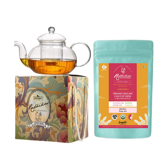 A Victorian glass kettle with a lid next to a packaged tea product, all presented on a decorative box with floral designs.