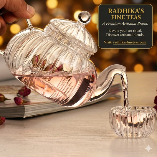 Clear glass tea infuser with floral elements being used to pour tea into a small glass container on a wooden surface.