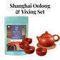 A bundle including a bag of Shanghai Oolong Tea and a set of Yixing teaware, with one visible red cup and a kettle on a mat, all against a white background.